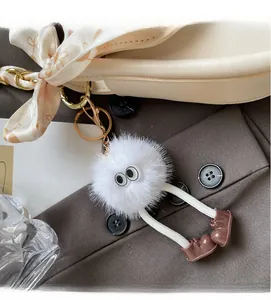 Détail d'un porte-clés monstre en peluche blanche accroché à un sac à main beige chic