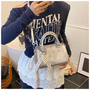 Detail of silver boston bag featuring pearl charm and white lace bow decoration