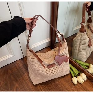 Close-up of beige woven tote bag featuring brown leather straps and a map-shaped charm