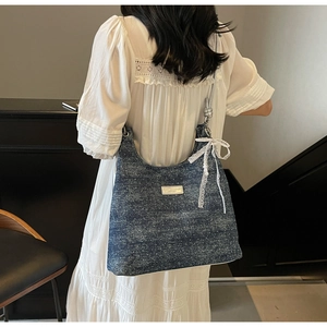 Blue denim hobo bag with white polka dots featuring a silver brand plate and lace bow