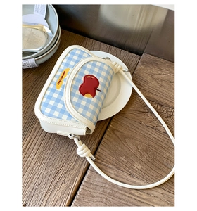 Detail view of light blue checkered saddle bag with red apple embroidery and knotted strap