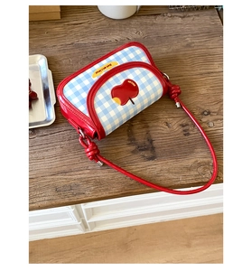 Detail of blue plaid saddle bag featuring red apple patch and decorative knotted strap