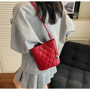 Gros plan sur un sac bandoulière rouge matelassé avec pendentif coeur porté par un mannequin