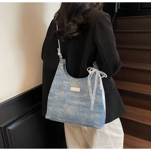 Close-up of a blue denim shoulder bag with lace bow and pearl pendant on a model