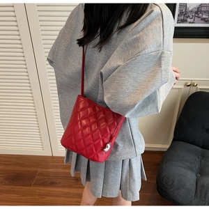 Détail du sac seau matelassé rouge avec breloque cœur sur un mannequin en gris