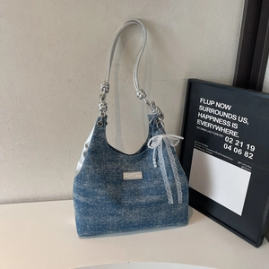 Close-up of denim hobo bag with silver metallic straps and a white lace bow charm