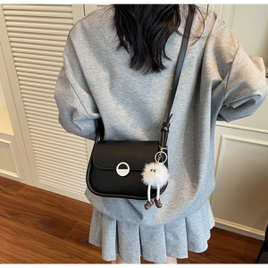 Détail du sac bandoulière noir avec boucle en métal argenté et pendentif en peluche blanc