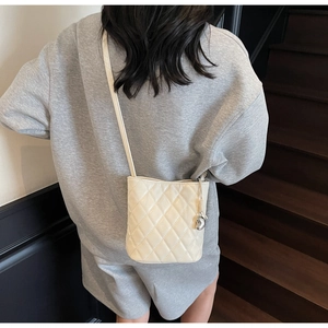 Vue détaillée du sac seau matelassé crème avec pendentif en métal élégant sur un mannequin
