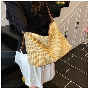 Detail view of woven straw tote bag with brown leather strap worn by a model