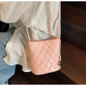 Détail d'un sac seau matelassé rose avec bandoulière porté dans un cadre décontracté