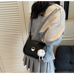Sacoche noire chic sur modèle avec breloque en peluche blanche et fermoir en métal