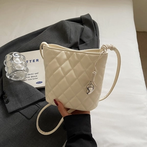 Gros plan du sac seau matelassé crème avec pendentif cœur en argent et bandoulière