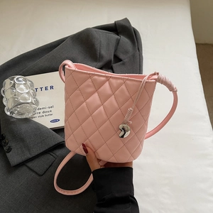 Détail d'un sac seau rose à motif matelassé en losanges avec pendentif cœur en métal