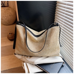 Detail of a large woven straw tote bag featuring black leather straps and a zipper closure