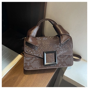 Détail du sac marron foncé avec gaufrage serpent et boucle noire sur une table