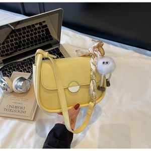 Détail d'un sac selle jaune avec foulard en soie, pendentif en peluche et fermoir