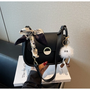 Détail de sac à bandoulière noir avec boucle métallique demi-lune et foulard en soie