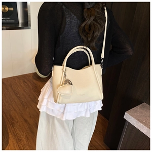 Détail d'un sac seau beige texture litchi avec pendentif cœur et bandoulière amovible