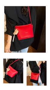 Dettaglio borsa a secchiello in pelle rossa con logo oro, ciondolo orsetto e nastro di seta