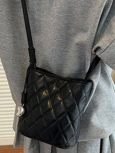 Sac seau matelassé noir avec pendentif cœur porté sur un sweat à capuche gris chiné