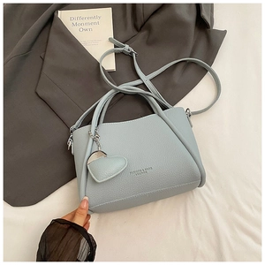 Détail du sac seau bleu clair motif litchi avec pendentif cœur sur literie blanche