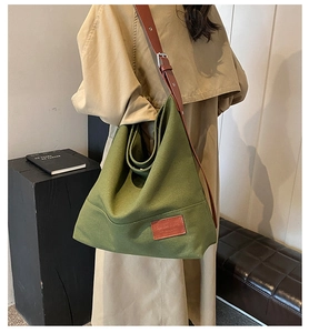 Detail of green canvas hobo tote bag featuring dark brown leather straps and chic logo patch