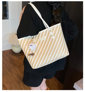 Detailed side view of a large woven tote bag with a white plush eye charm and branding