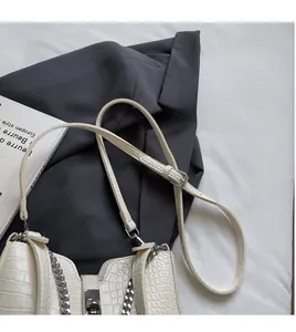 Detail of off-white crocodile embossed crossbody bag with metal lock and silver chain