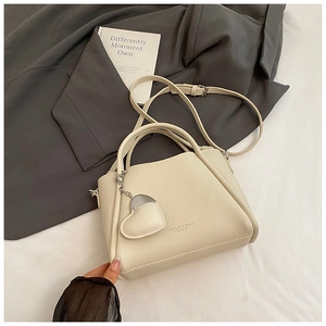 Gros plan du sac seau en cuir grainé blanc cassé avec pendentif cœur et bandoulière