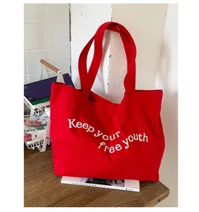 Close-up of red canvas tote bag with white Keep Your Free Youth embroidery detail