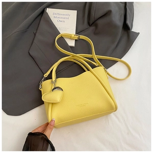 Détail du sac seau jaune à motif litchi avec pendentif cœur sur fond de blazer gris