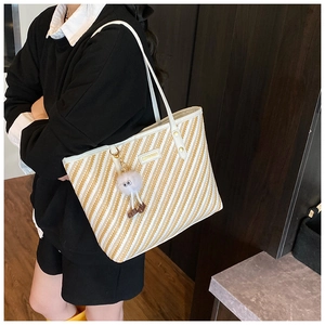 Detail of striped woven straw tote bag with thin shoulder strap and plush charm decoration