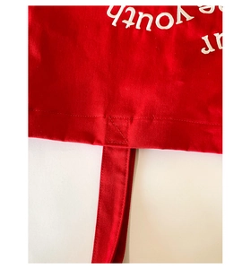 Detailed close-up of reinforced cross-stitching on the red canvas tote bag handle