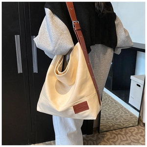 Detail of cream canvas tote bag with brown adjustable leather strap and logo patch