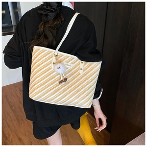 Detail of yellow striped woven tote bag with white strap and cute pompom accessory