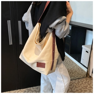 Detailed side view of a large cream canvas tote bag with brown leather strap on model