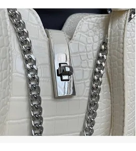 Detail of silver twist lock and crocodile pattern leather on white shoulder bag