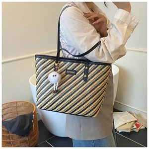 Detail of striped woven tote bag with leather handles and decorative plush doll charm