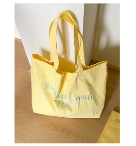 Close-up of blue embroidery lettering Keep Your Free Youth on yellow canvas tote bag