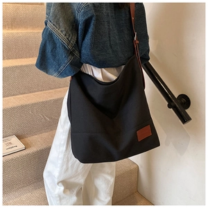 Detail of black canvas hobo bag with adjustable brown leather strap and square logo patch