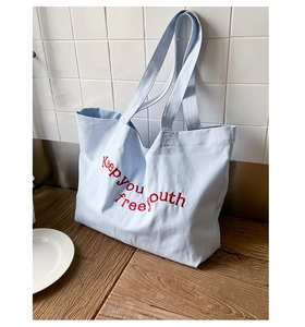Detail of light blue canvas tote bag with red embroidered 'Keep you free youth' text