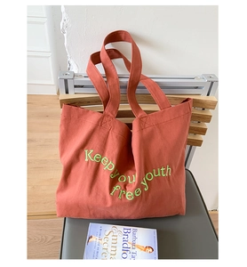 Detail of brick red canvas tote bag with Keep your free youth green embroidery