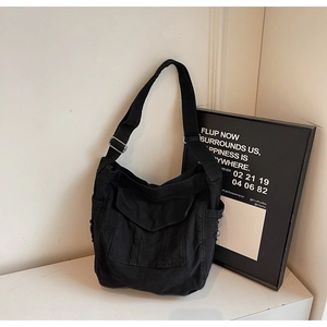 Macro detail of black denim shoulder bag featuring raw edges and utility pockets