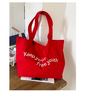 Macro detail of red canvas tote bag showing wide straps and white printed youth slogan