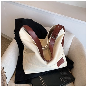 Detail of canvas hobo bag with brown leather straps and silver buckle on white chair