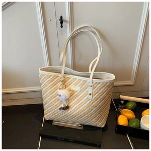 Detailed close-up of striped straw tote bag featuring white faux leather trim and plush charm
