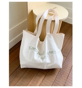 Close-up of green 'Keep your youth free' embroidery on a white canvas tote bag