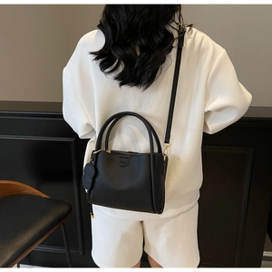 Détail du sac seau en cuir grainé noir avec pendentif chien et logo de mode gravé