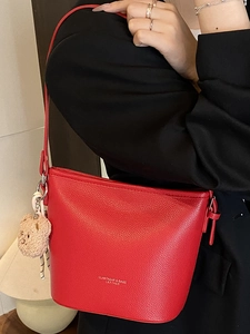Borsa a secchiello in pelle rossa con ciondolo a orso indossata da modella in tailleur