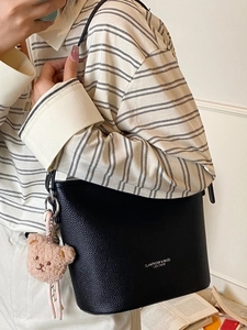 Borsa a secchiello nera minimalista trama litchi con ciondolo orsetto indossata a spalla
